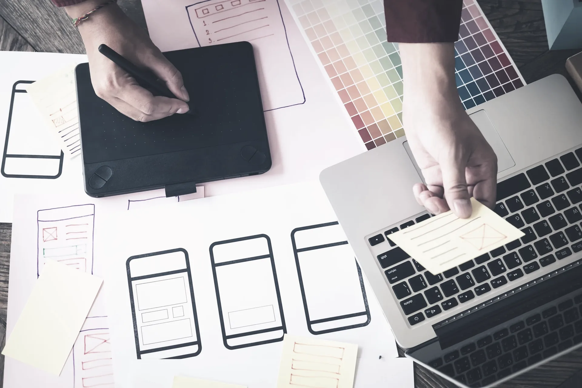 Wireframes, colour swatches and devices on a designer's desk